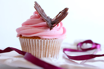 vanilla cupcake with pink frosting and a chocolate butterfly on a white background