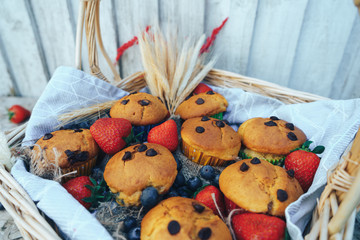 Basket of vegan chocolate chip muffins on the pattern cloth, strawberry and blueberry in basket and on  wooden table. Selective focus.