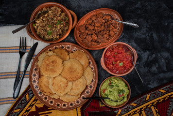 Vegan Mexican gorditas along with refried beans, guacamole, tomato salsa and fried seitan pieces in traditional Mexican bowls
