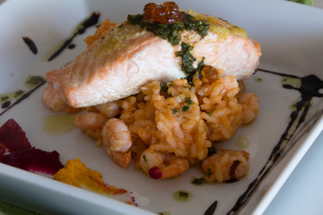 grilled salmon on tomato rice and prawns presented on white plate