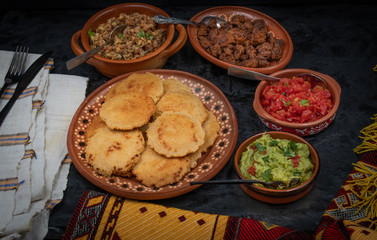 Vegan Mexican gorditas along with refried beans, guacamole, tomato salsa and fried seitan pieces in traditional Mexican bowls