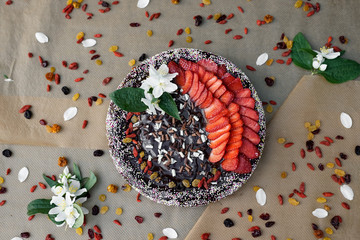 Fototapeta premium Homemade strawberry cheese cake with raisins and dry fruits, triple chocolate curls, multi coloured sugar with chocolate topping on brown baking paper with dry fruits and flower of jasmine. Flat lay.