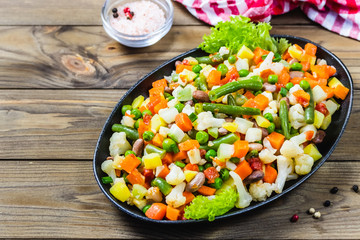 Sauteed vegetables, beans, cauliflower, carrot, pumpkin  in cast iron skillet on wooden background.