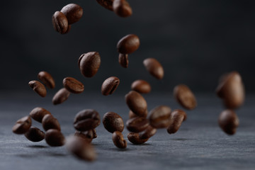 Many roasted coffee beans flying in the air. Selective focus. Coffee beans on a background of gray granite wall and table