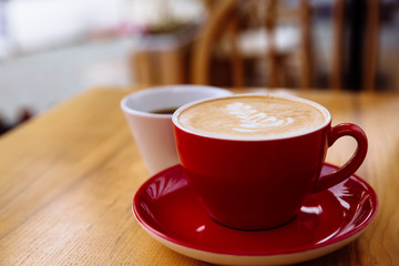 Coffee in a red cup with milk and latte art and coffee in a white cup on a table