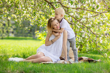 Family mother and son, beautiful and happy together sitting on the grass in front of a flowering Apple tree