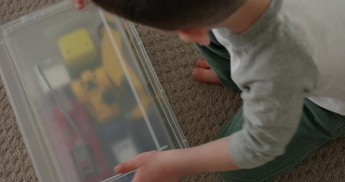 Toddler boy putting toy cars away in box then closing the lid - from above - close up