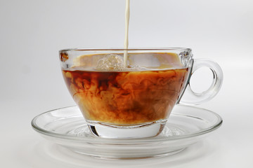 dark Coffee poring white milk dripping splash shadow liquid swirl in glass cup saucer on white background