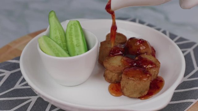 Pouring sweet and spicy sauce on top of Deep Fried Crab Meat Rolls or Hoi Jo or Deep-fried spring rolls , goodie crab roll or crab jujube in a white plate ,Traditional local Chinese food for appetizer