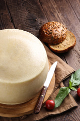 Cheesemaking. Homemade cheese on a wooden board on an old wooden background with a knife, basil, tomatoes, bread and spices. Rustic. Background image, copy space