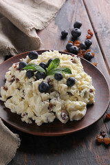 Fermented milk product. Cottage cheese  with raisins and blueberries in a clay plate on an old wooden background. Curd mass, fresh berries. Rustic. Background image, copy space