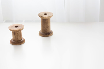 Vintage french wooden empty sewing reels on a white wooden surface against a white curtains background. free space for your inscription