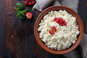 Fermented milk product. Homemade cottage cheese in a clay bowl with berries: strawberries, red currants, mint an old wooden background. Rustic. Flatlay, top view. Background image, copy space