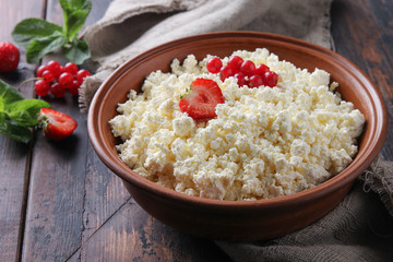 Fermented milk product. Homemade cottage cheese in a clay bowl with berries: strawberries, red currants, mint on an old wooden background. Rustic. Background image, copy space