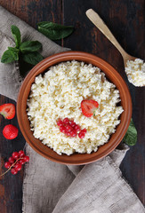 Fermented milk product. Homemade cottage cheese in a clay bowl with berries: strawberries, red currants, mint and a spoon on an old wooden background. Flatlay, top view. Background image, copy space