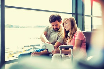 Portrait of young beautiful teenage girl showing digital tablet to her father while sitting and waiting for their flight in airport
