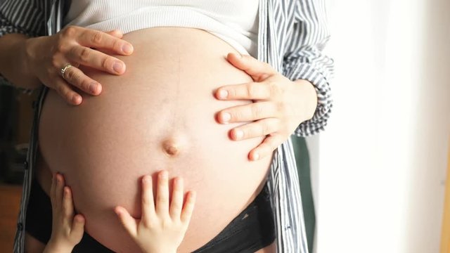 little girl older sister touching pregnancy belly, chlidren hands boy brother siblings