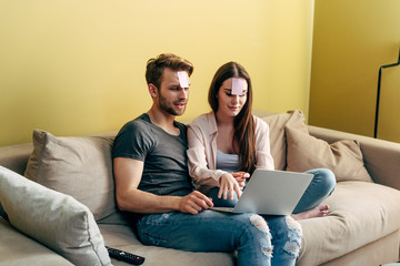 couple with sticky notes on foreheads playing online game near laptop