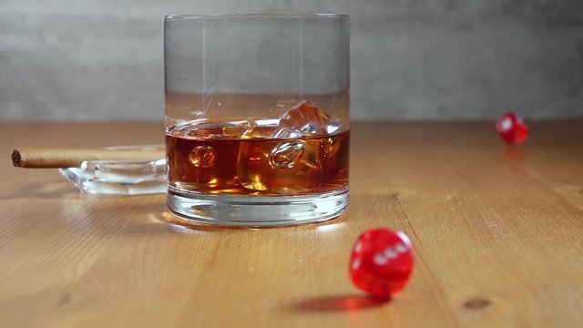 Glass of Whiskey on a Wooden Table and Dice. Slow Motion