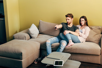 bearded man watching movie near girlfriend, laptop and digital tablet with blank screen on coffee table