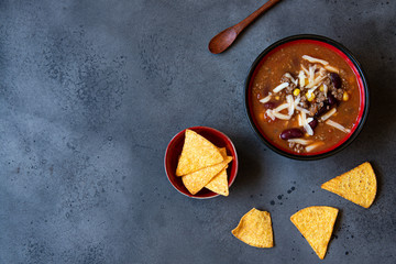 chilli con carne soup with wooden spoon and nachos. top view, copy space, neutral grey background