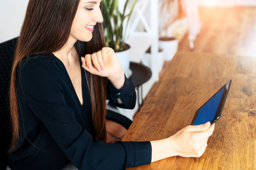 Beautiful young woman in black smart casual shirt with a digital tablet in hands in the office. Side view