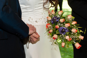 
clasped hands of two bride and groom at a wedding with bouquet of flowers assuming a love pact