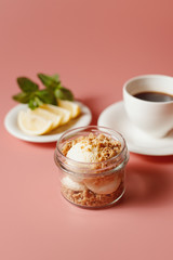 ice cream with crumble, next to a cup of coffee and sliced lemon on a pink background