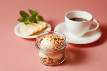 ice cream with crumble, next to a cup of coffee and sliced lemon on a pink background