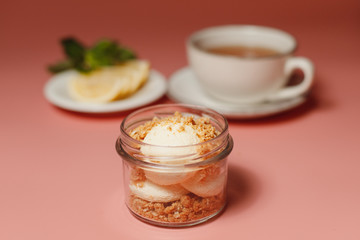 ice cream with crumble, next to a cup of tea and sliced lemon on a pink background