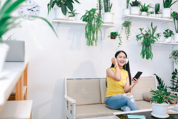 A beautiful Asian woman in a coffee shop enjoying listening to music on her mobile phone and...