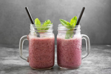 Berry smoothie in glass jar with mint leaves, grey background.