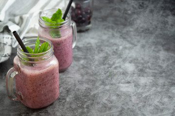 Berry smoothie in glass jar with mint leaves, grey background.