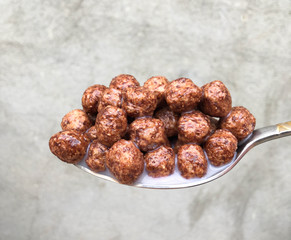 full spoon of chocolate cereal on a gray background for breakfast. Sweet cocoa, chocolate, sugar, cereal, puffs with milk.