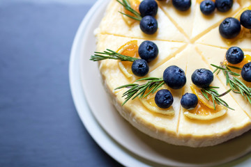 Homemade cheesecake with fresh blueberry and candied lemon on black stone background.