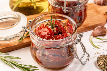 Food recipe background. Close up Sun dried tomatoes with garlic, oregano, olive oil in a jar on a light table, top view