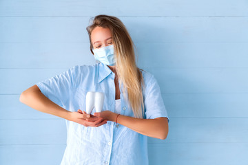 Human molar tooth Model. Female dentist in blue uniform holding tooth on blue background. Oral care...