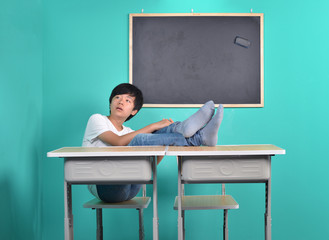 Young Asian school boy in classroom with feet on table