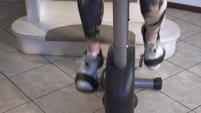 women's legs in white sneakers and sweatpants quickly twist the pedals of a home exercise bike.