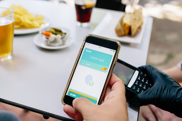 Contactless payment from a smartphone to a TPV terminal in a restaurant. Detail of hands and electronic devices.