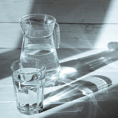 Shadows from the carafe and a glass of water on a white wooden background