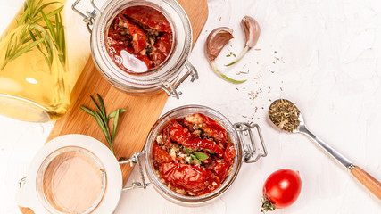 tomato dried tomatoes, dried tomatoes in jar, basil, and herbs in spoon on a light table. top view. Long banner format. space for text