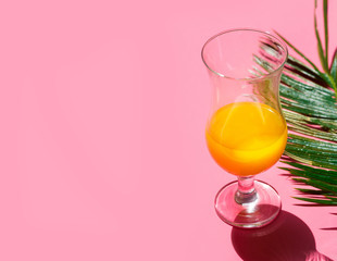 Half full cocktail glass with fresh tropical citrus fruits juice green palm leaf on fuchsia pink background. Summer vacation relaxation fashion travel concept. Funky pop art style