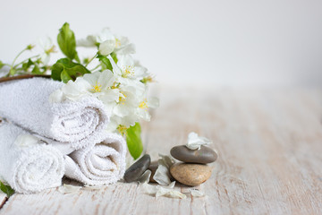 Obraz na płótnie Canvas Three white towels rolled up in a roll, a flowering branch with white flowers and natural stones on a light wooden table. Spa and beauty treatment concept. Copy space for text.