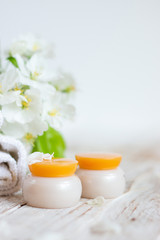 Two jars of face cream, white towels on a light wooden background. Spa and beauty treatment concept. Copy space for text.