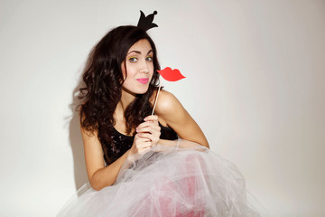 Portrait of young attractive woman sitting like a princess with a paper crown and paper red lips on...