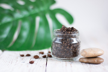 Ground coffee, sugar and butter scrub in a glass jar on a light wooden table. Homemade peeling and spa care product. Copy space for text.