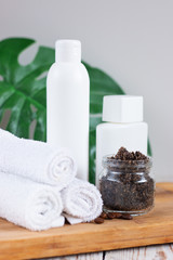 Fototapeta na wymiar Handmade coffee scrub in a glass jar on a light wooden table. White towels rolled up and bottles with cosmetic. The concept of home care and spa treatments.