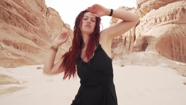 Redhead girl in black suit practice ecstatic dance in desert