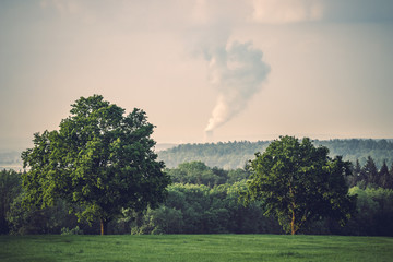Green landscape with cooling tower of a nuclear power plant emitting steam to the sky. Sad, dark...